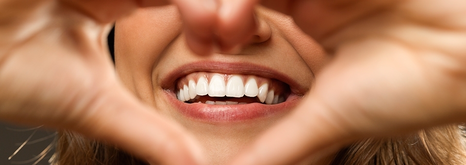 kvinder laver hjerteform med sine hænder over sin mund mens hun smiler - pænt smil med tandlæge